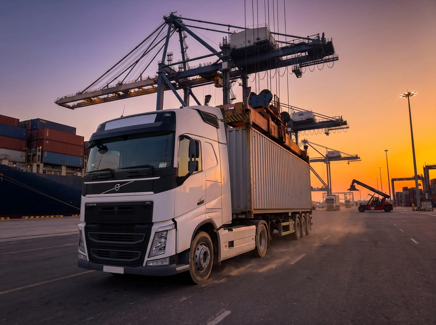 White truck carrying a shipping container under gantry cranes at a UAE port terminal